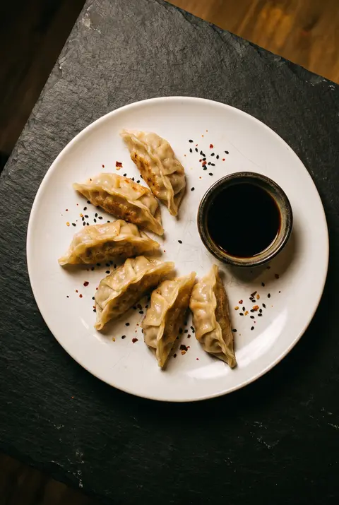 Six pan fried pork dumplings with a small dish of soy dipping sauce on a white plate