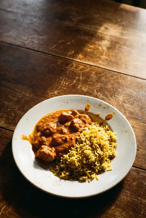 A portion of chicken tikka masala beside a portion of pilau rice on a white plate