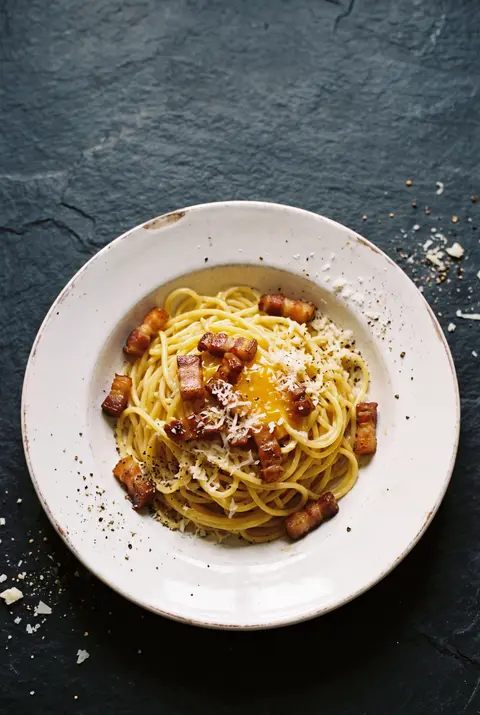 A restaurant plate of spaghetti carbonara with crisp guanciale on a white plate