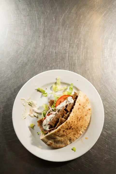 A doner kebab in a pitta with salad and garlic sauce on a white plate