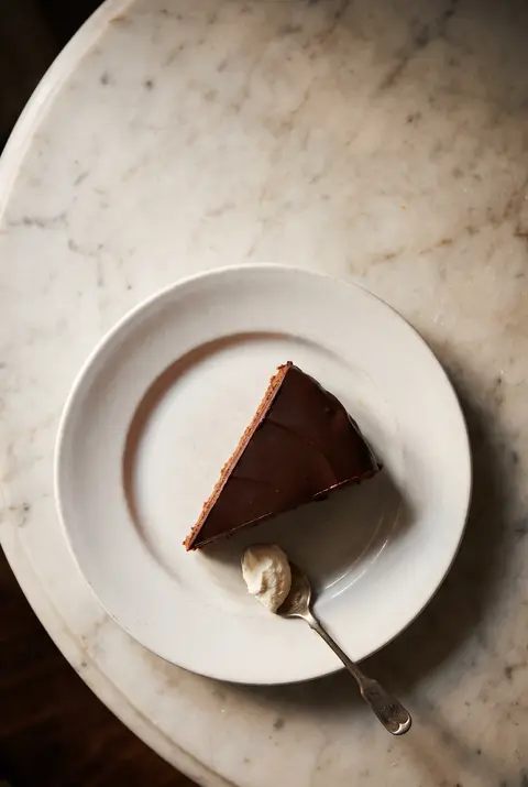 A slice of Sachertorte with a dark chocolate glaze and a thin apricot layer on a white plate