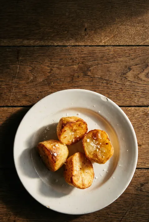 About four crisp golden roast potatoes on a white plate