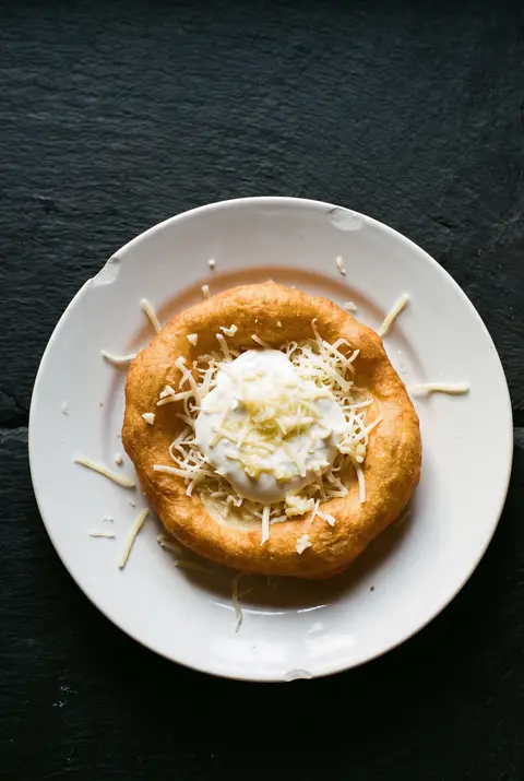 A golden Hungarian langos topped with sour cream on a white plate