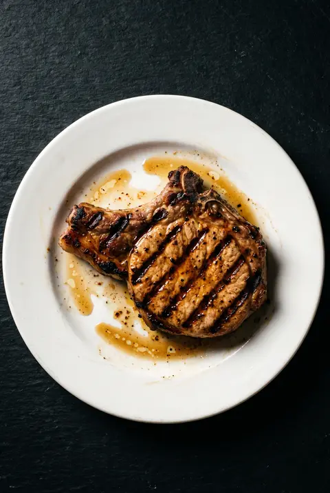 A grilled pork chop with grill marks on a white plate