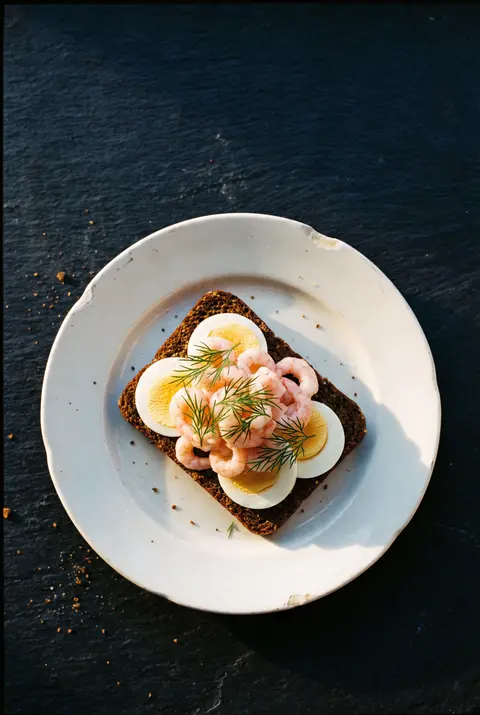 A Danish open sandwich on dark rye bread with egg on a white plate