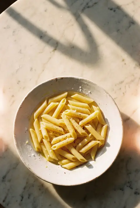 A plate of plain cooked penne pasta with no sauce on a white plate