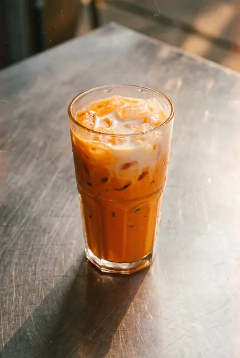 350 ml of bright orange Thai iced tea with ice and a layer of milk on top in a clear glass