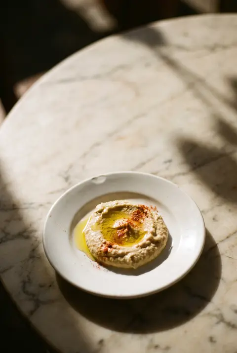 Two tablespoons of hummus with a swirl of olive oil on a white plate