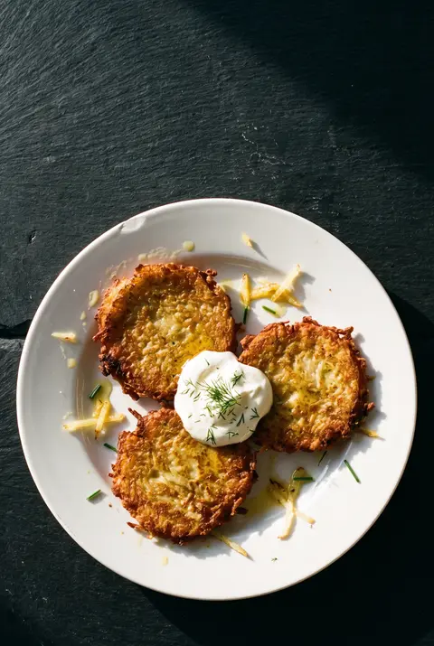 Three golden potato pancakes with a spoonful of sour cream on a white plate