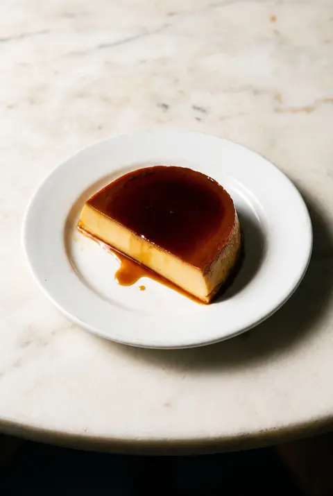 A slice of leche flan with dark caramel on top on a white plate