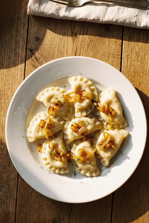 Eight pierogi ruskie topped with golden fried onion on a white plate