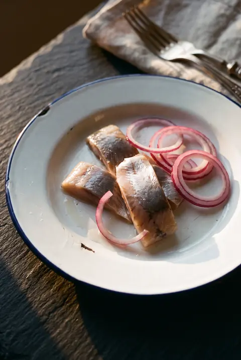 A few pieces of pickled herring with red onion rings on a white plate