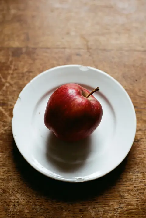 A crisp red apple with a short stem on a white plate