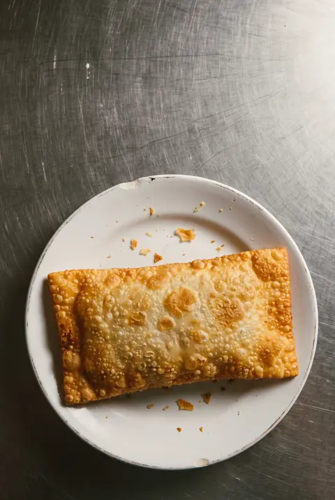 A large rectangular fried Brazilian pastel with blistered crust on a white plate