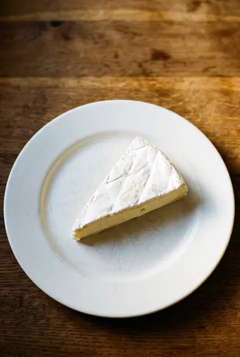 A wedge of brie with a soft white rind on a white plate