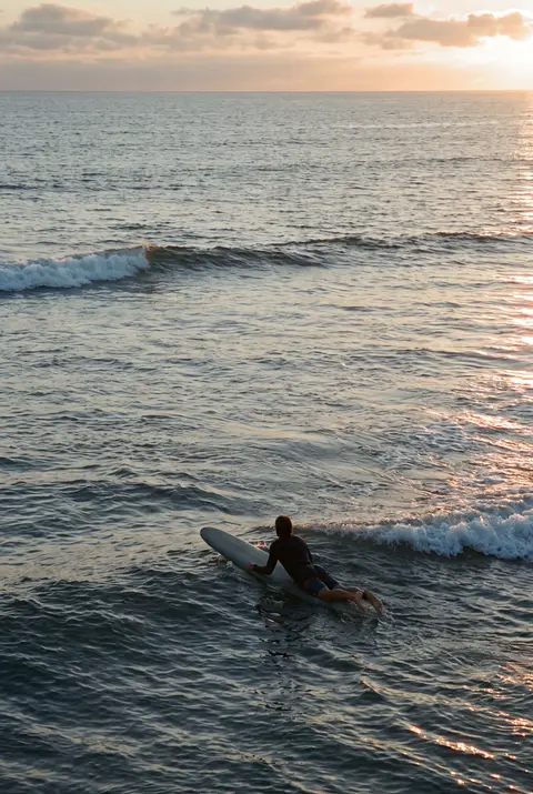 One surfer paddling out on a board on a calm sea with small breaking waves