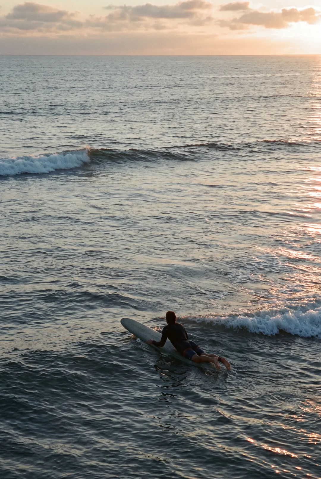 One surfer paddling out on a board on a calm sea with small breaking waves