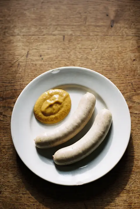 Two Bavarian white sausages with a spoonful of sweet mustard on a white plate