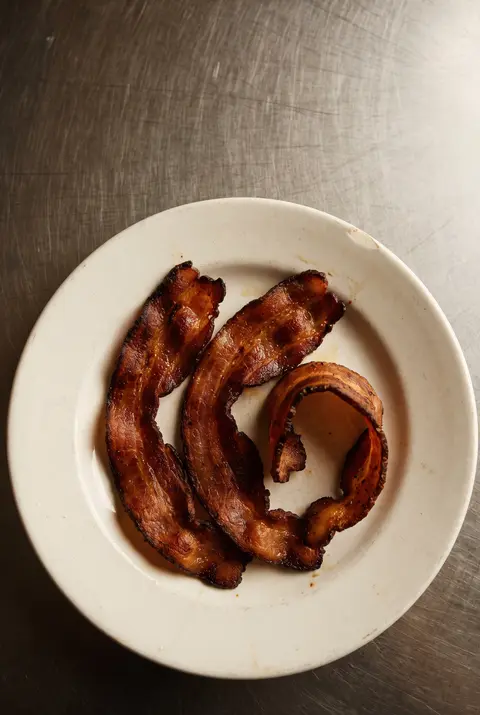 Three crisp cooked rashers of bacon on a white plate