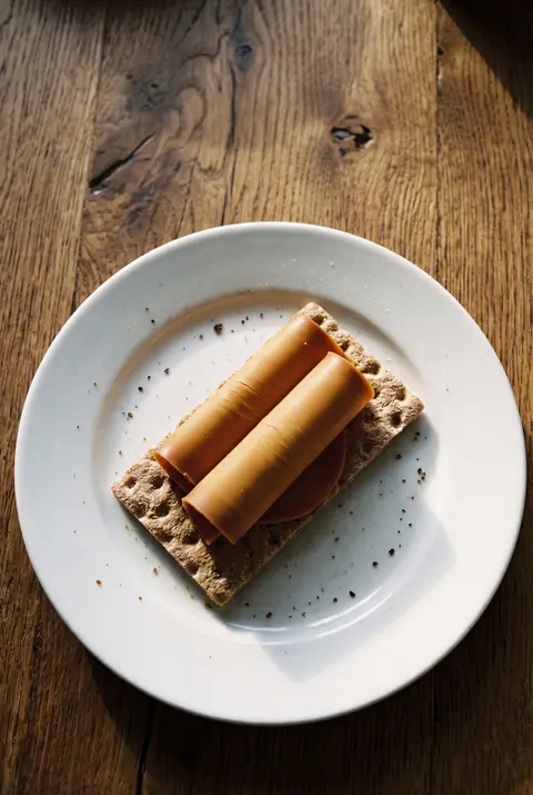 A few thin slices of brown brunost cheese on a crispbread on a white plate