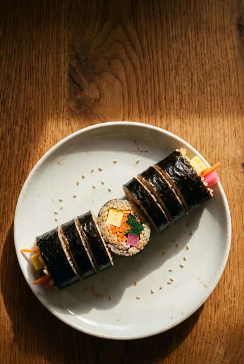 A whole gimbap roll cut into slices showing rice on a white plate