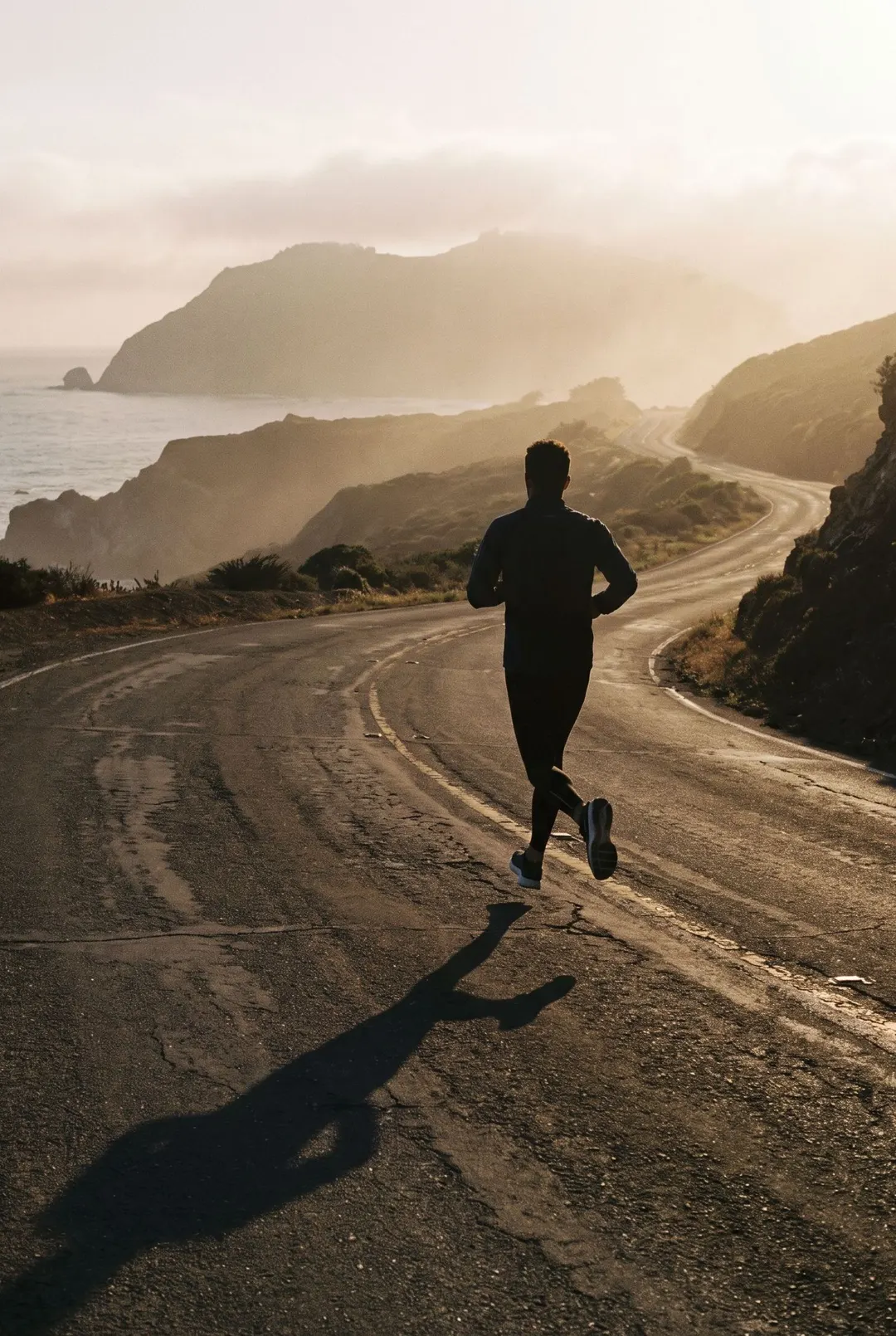 One runner mid stride on an empty coastal road in early morning light