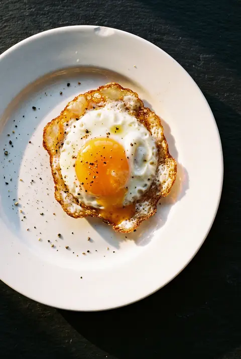 A fried egg with a runny yolk and crisp edges on a white plate