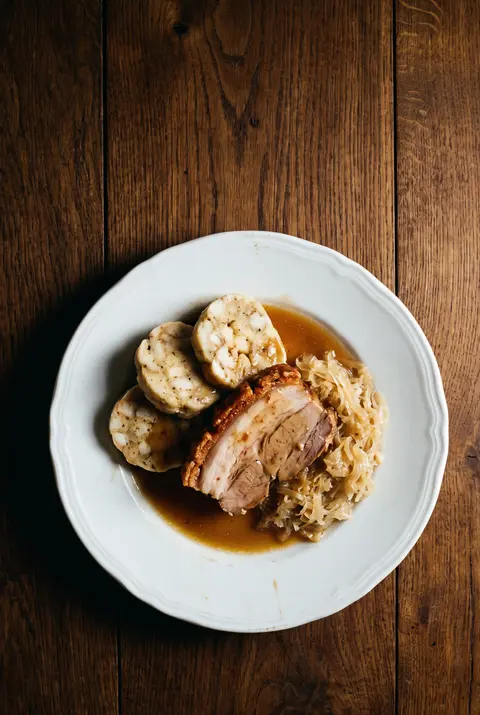 A plate of roast pork with bread dumplings and braised sauerkraut on a white plate