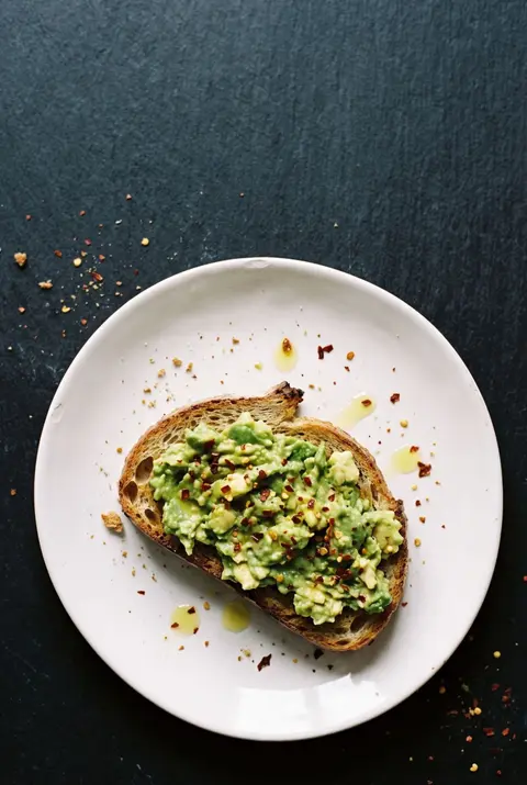 A slice of sourdough toast with smashed avocado and chili flakes on a white plate