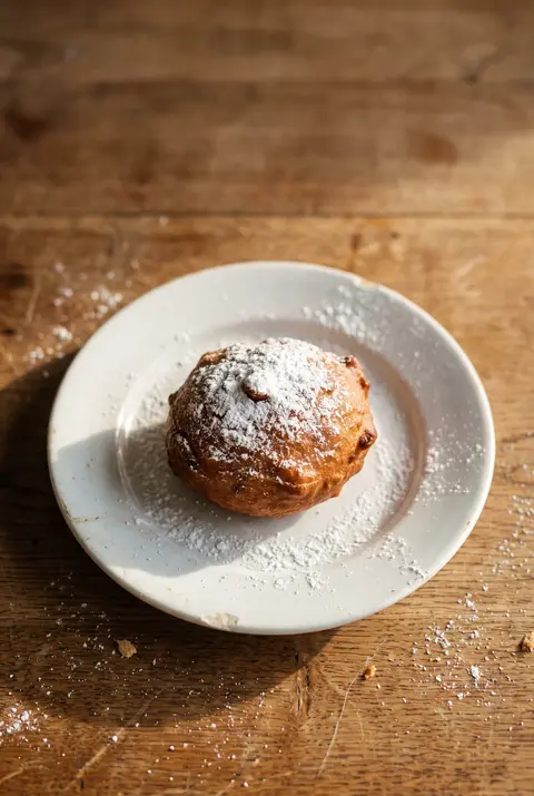 A Dutch oliebol dusted with powdered sugar on a white plate