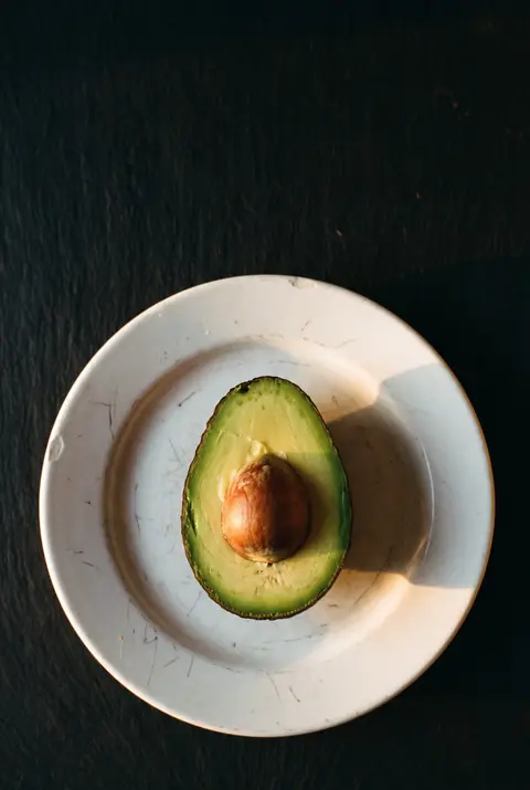 Half a ripe avocado with the stone still in on a white plate