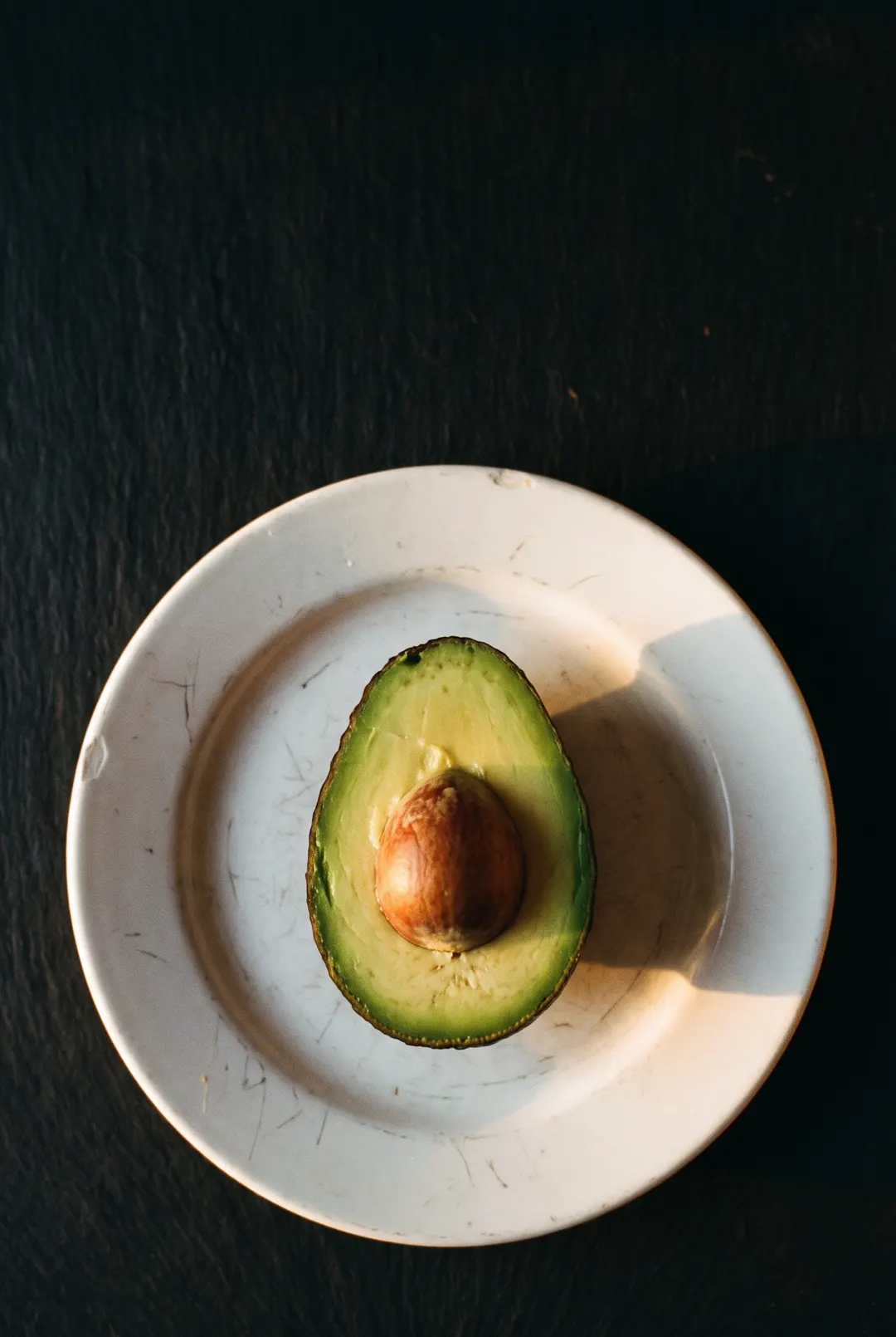 Half a ripe avocado with the stone still in on a white plate