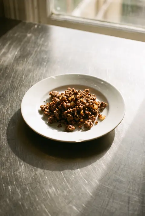 100 g of browned cooked minced beef on a white plate