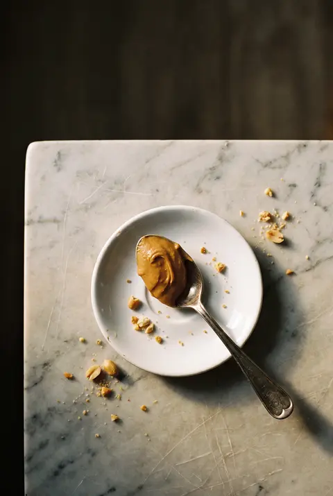 A tablespoon of smooth peanut butter on a small white porcelain spoon on a white plate