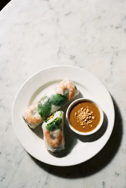Two Vietnamese summer rolls with prawns and herbs showing through rice paper on a white plate