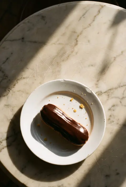 A chocolate eclair with a dark chocolate top on a white plate