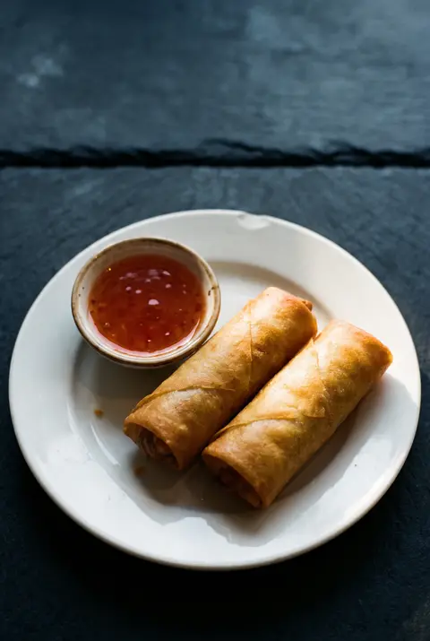 Two golden fried spring rolls with a small dish of sweet chili sauce on a white plate