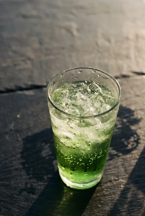 A green energy drink with ice and fine bubbles in a clear glass