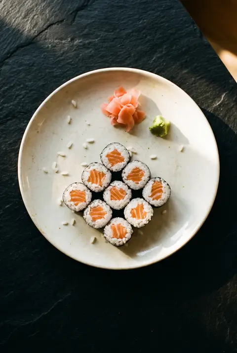 Eight pieces of salmon maki roll with a little pickled ginger and wasabi on a white plate