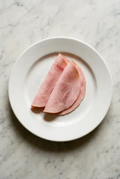 Two thin slices of cooked ham on a white plate