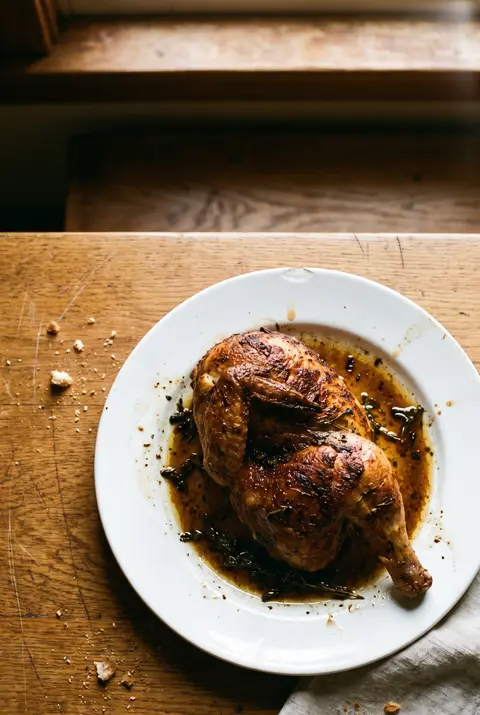 Half a roast chicken with crisp golden skin on a white plate