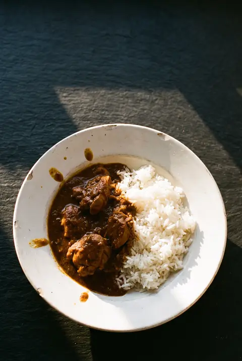 A portion of chicken curry beside a portion of white rice on a white plate