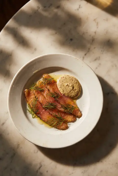 About 75 g of thinly sliced gravlax with dill and a little mustard sauce on a white plate