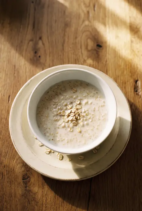 A white porcelain bowl of creamy porridge made with milk on a white plate