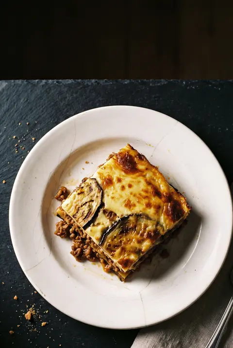 A square portion of moussaka showing layers of aubergine on a white plate
