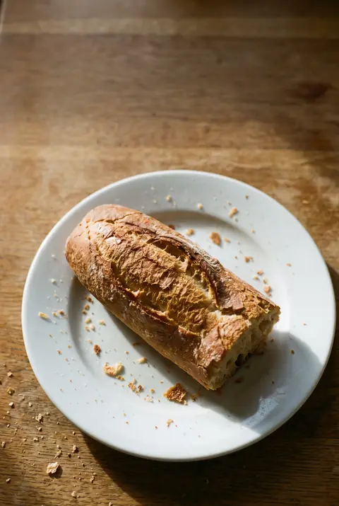 Half a crusty baguette with a golden crust on a white plate