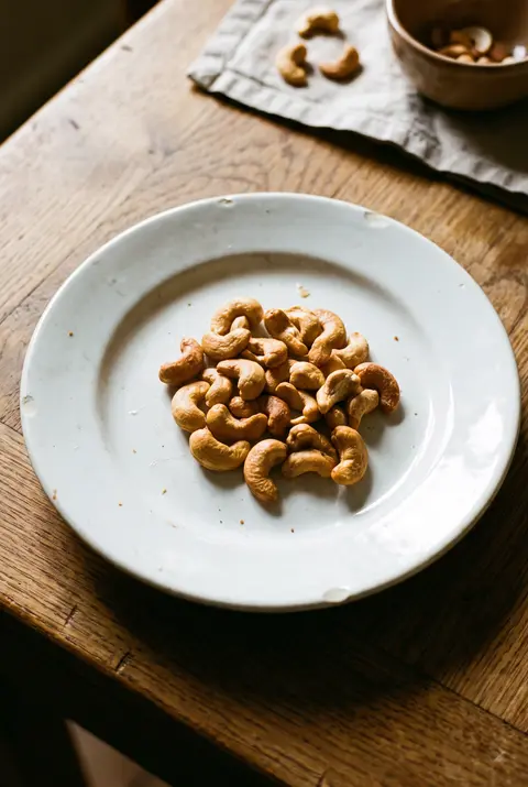 A small heap of roasted cashews on a white plate