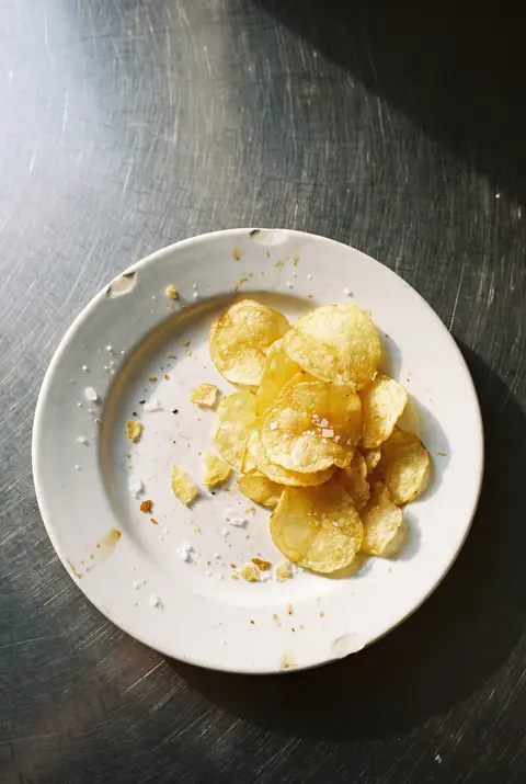 A small pile of thin golden potato crisps on a white plate