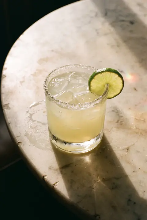 A classic margarita on the rocks with a salted rim and a wedge of lime in a short rocks glass