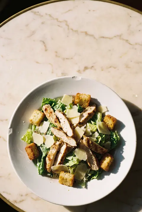 A main size chicken Caesar salad with croutons and shaved parmesan on a white plate
